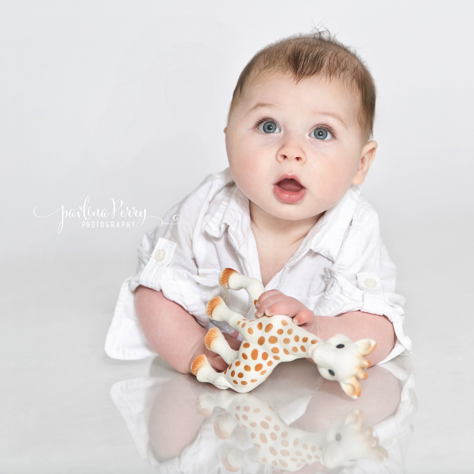 Baby in a white shirt holding a giraffe toy in a bright studio