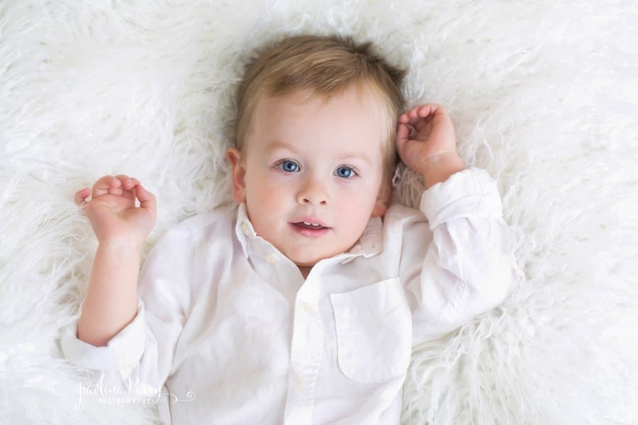 Baby lying on a white blanket wearing a white shirt