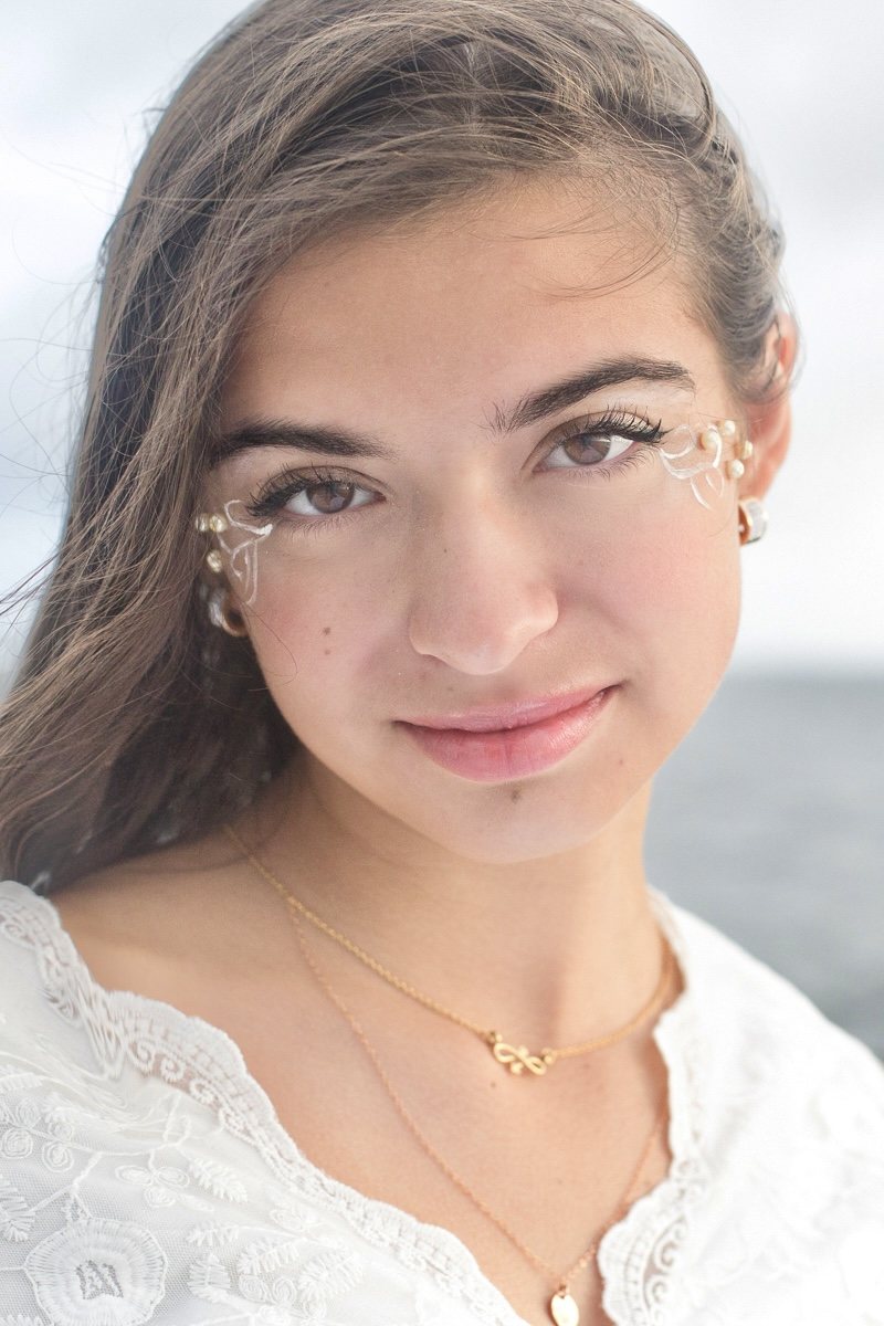 Close-up portrait looking toward the camera, with delicate pearl details beside her eyes