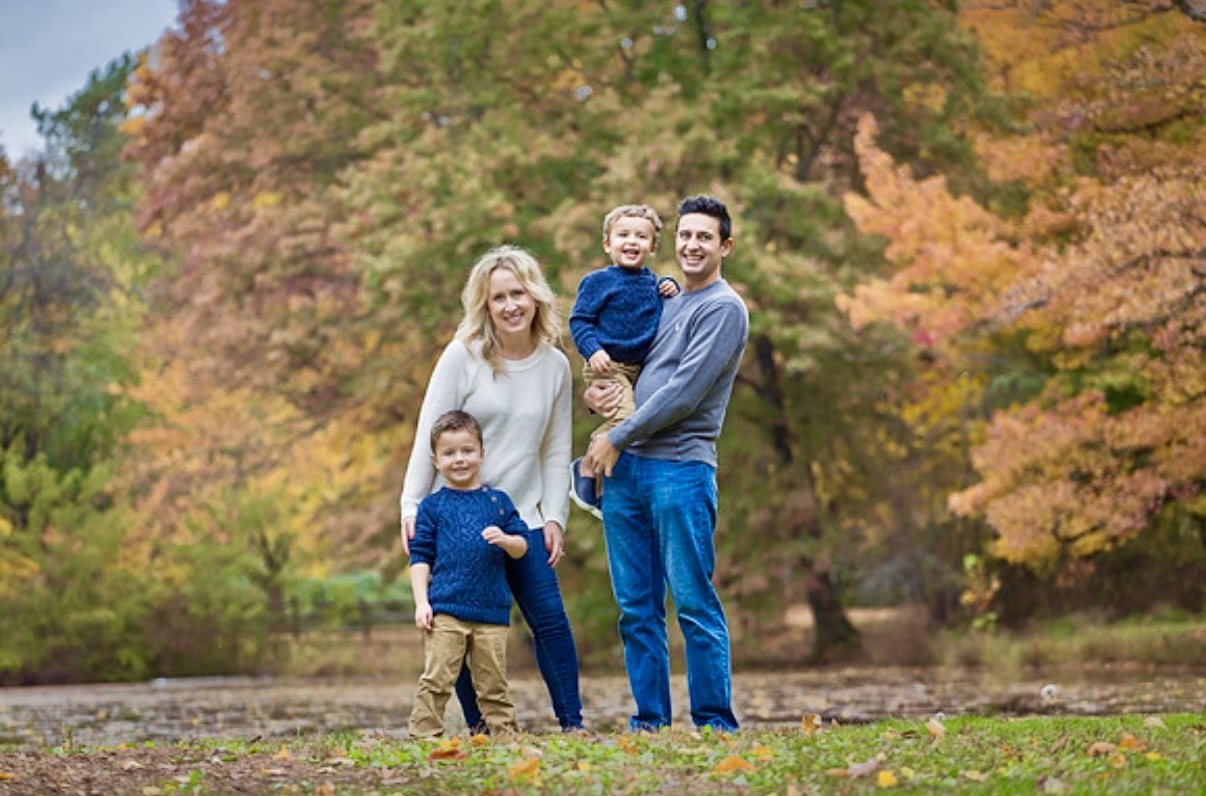Parents with their two young boys beside a lake surrounded by autumn foliage.