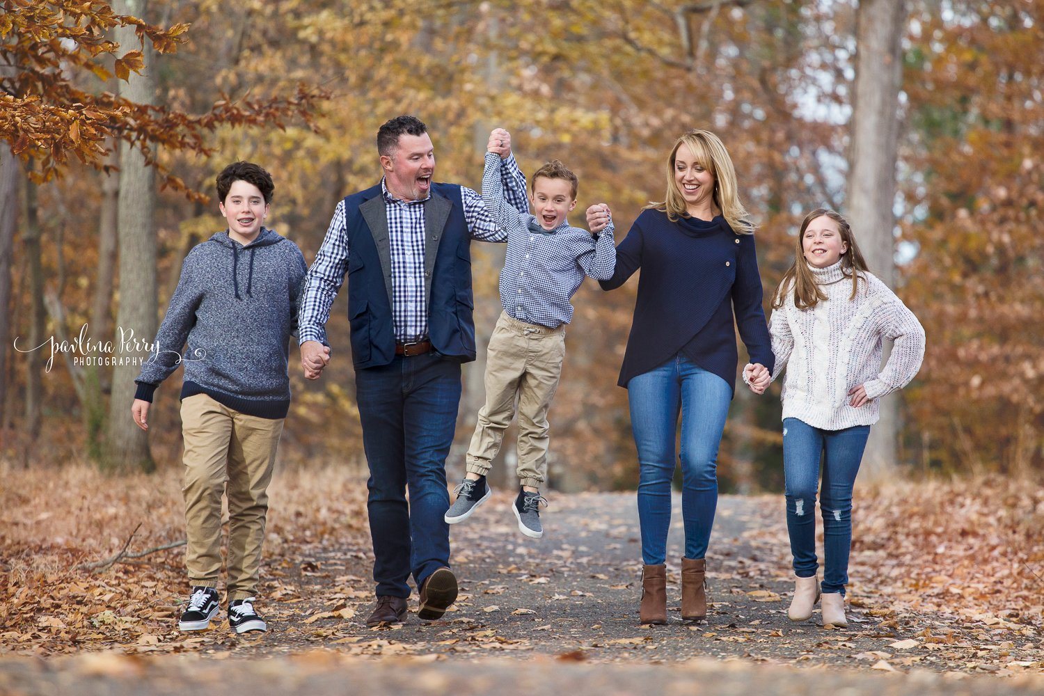 Family of five walking and laughing on an autumn woodland path