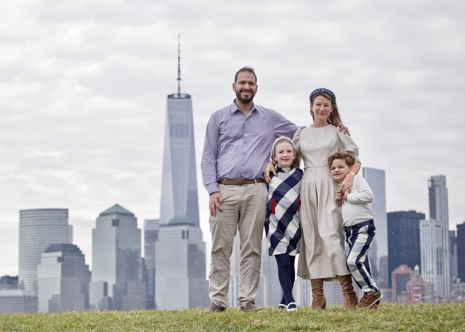 Family of four standing on grass with the Manhattan skyline behind them.