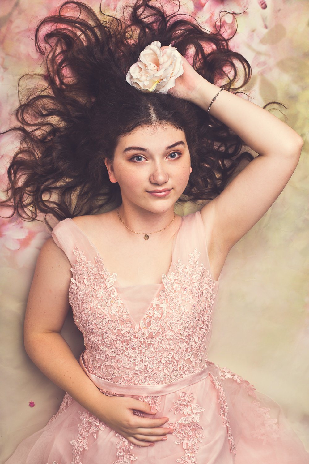 Portrait of a young woman in a pink lace dress holding a flower with her hair spread around her