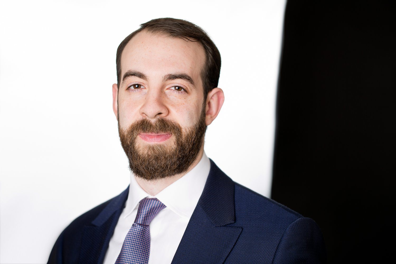 Professional headshot of a bearded man wearing a navy suit and tie