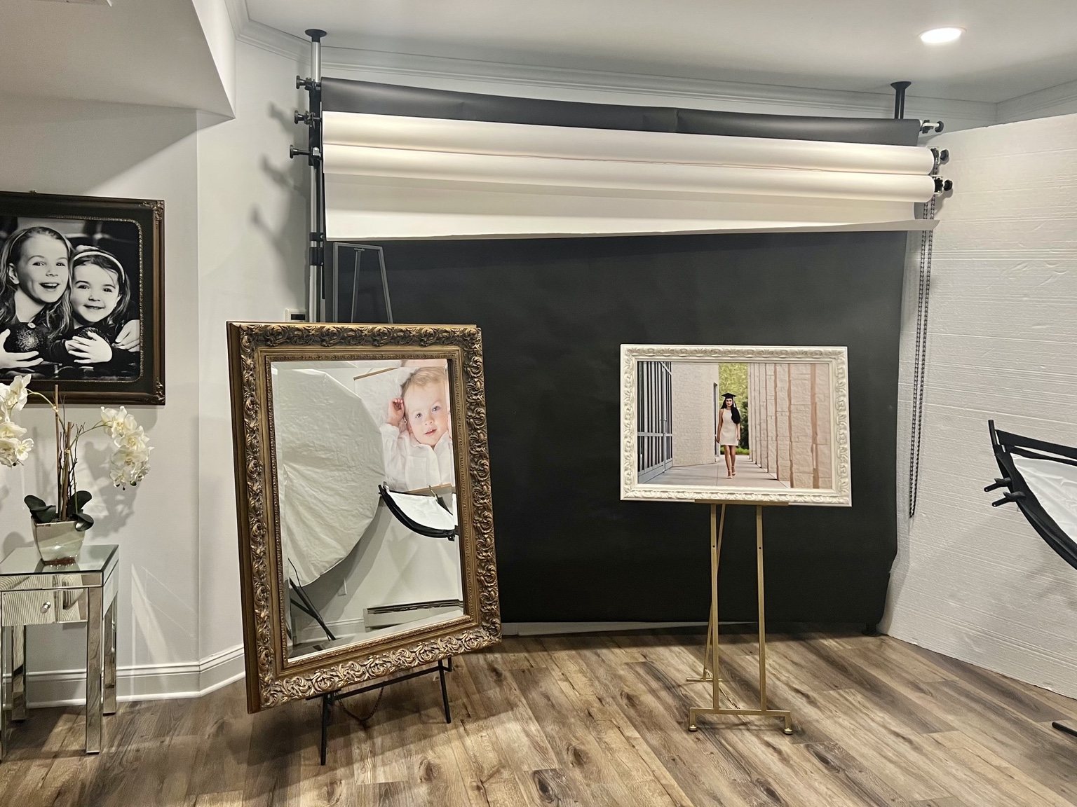Pavlina’s studio with portrait backdrops, framed photographs, an ornate mirror, and a graduation portrait on an easel