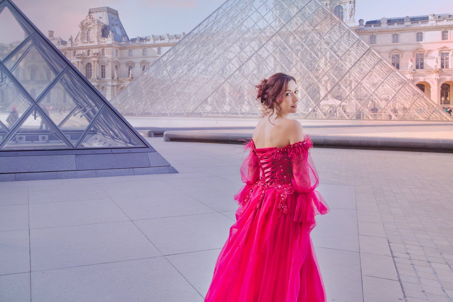 Woman in a vivid pink gown in front of the Louvre pyramids