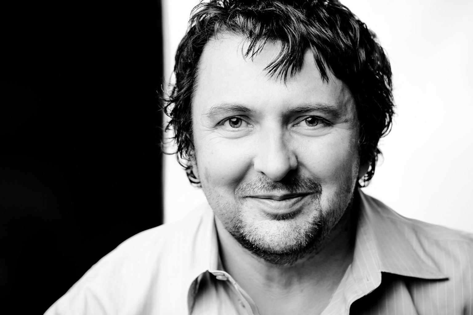Black-and-white close headshot of a man in an open-collar shirt