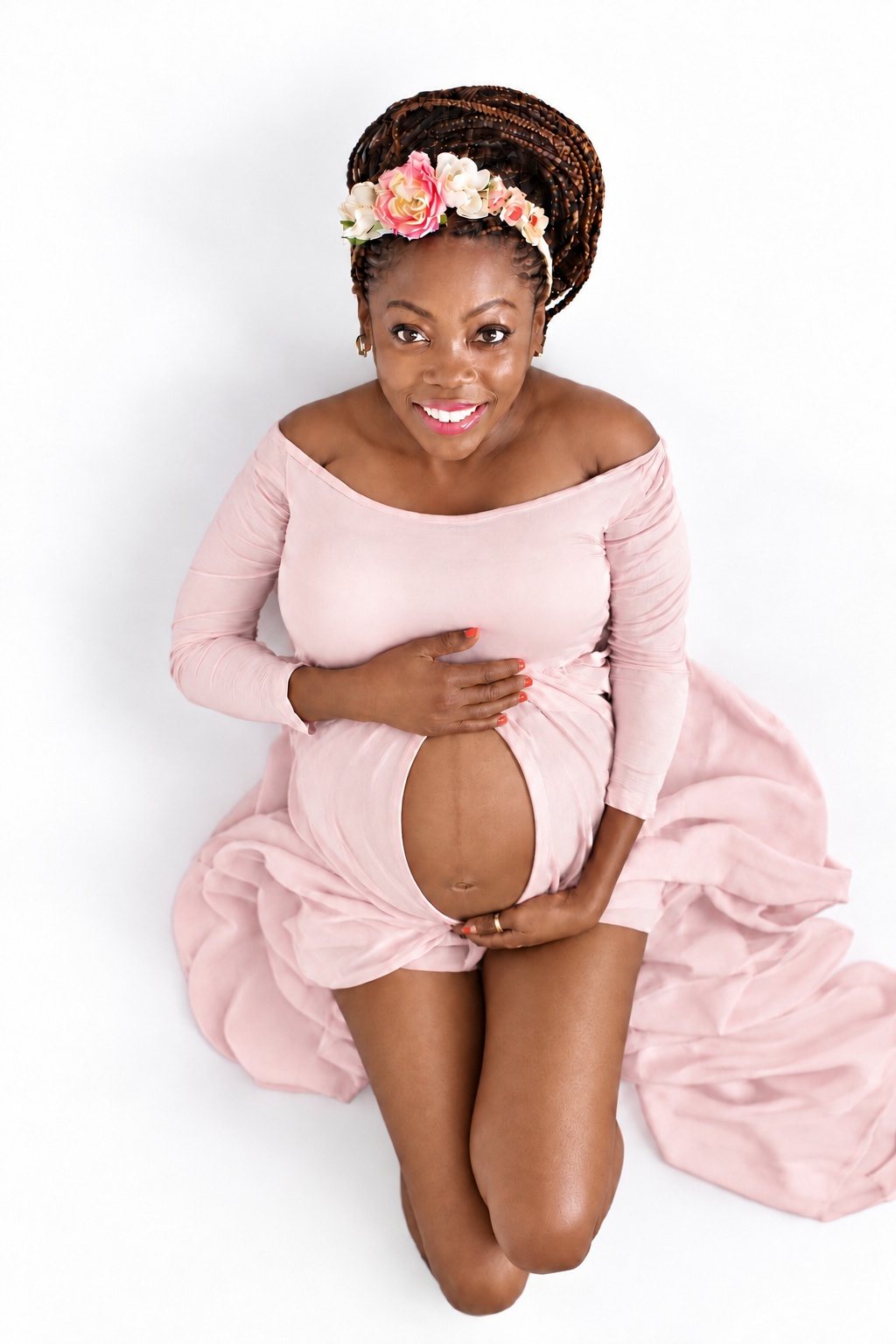Maternity portrait photographed from above, with a woman in a pink gown and floral crown holding her belly