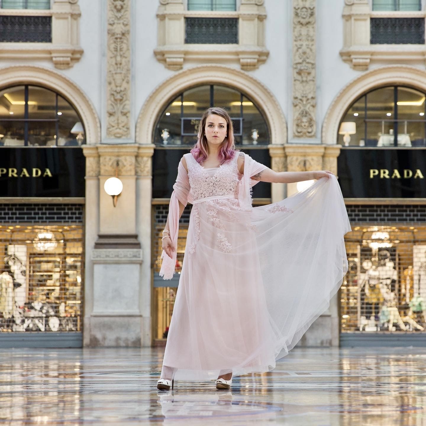 Woman holding out her pale pink gown beneath ornate stone arches