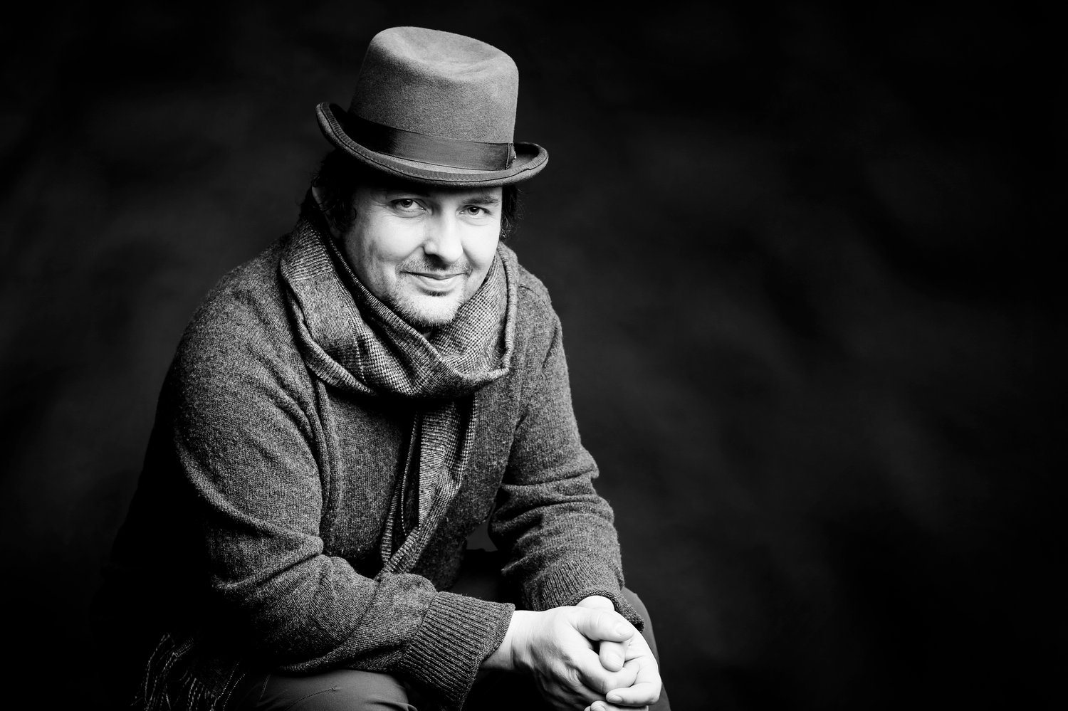 Black and white portrait of a man in a hat and scarf against a dark background