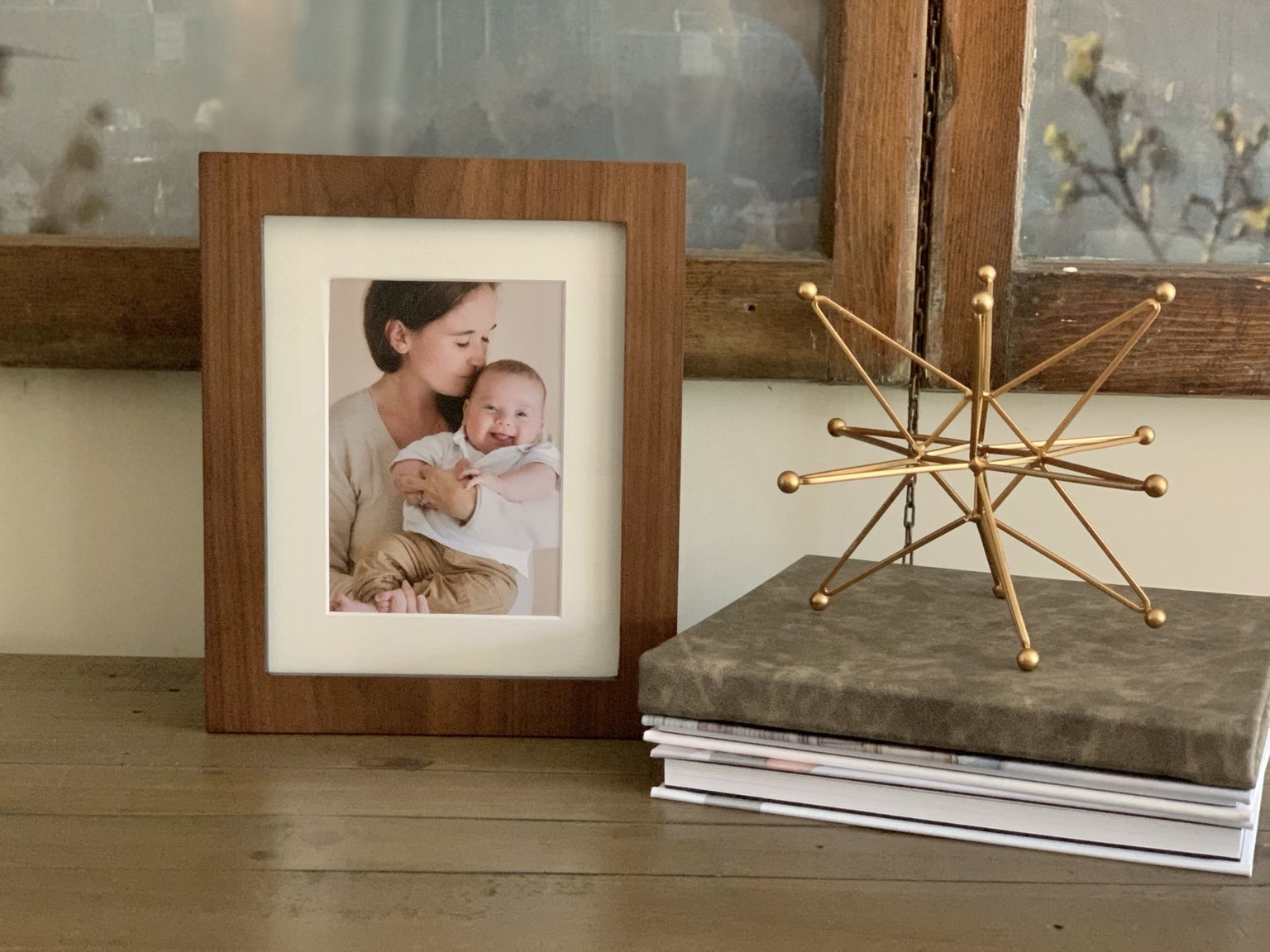 Wooden frame with a mother and baby portrait beside Pavlina’s real fabric-covered folio box and matted prints