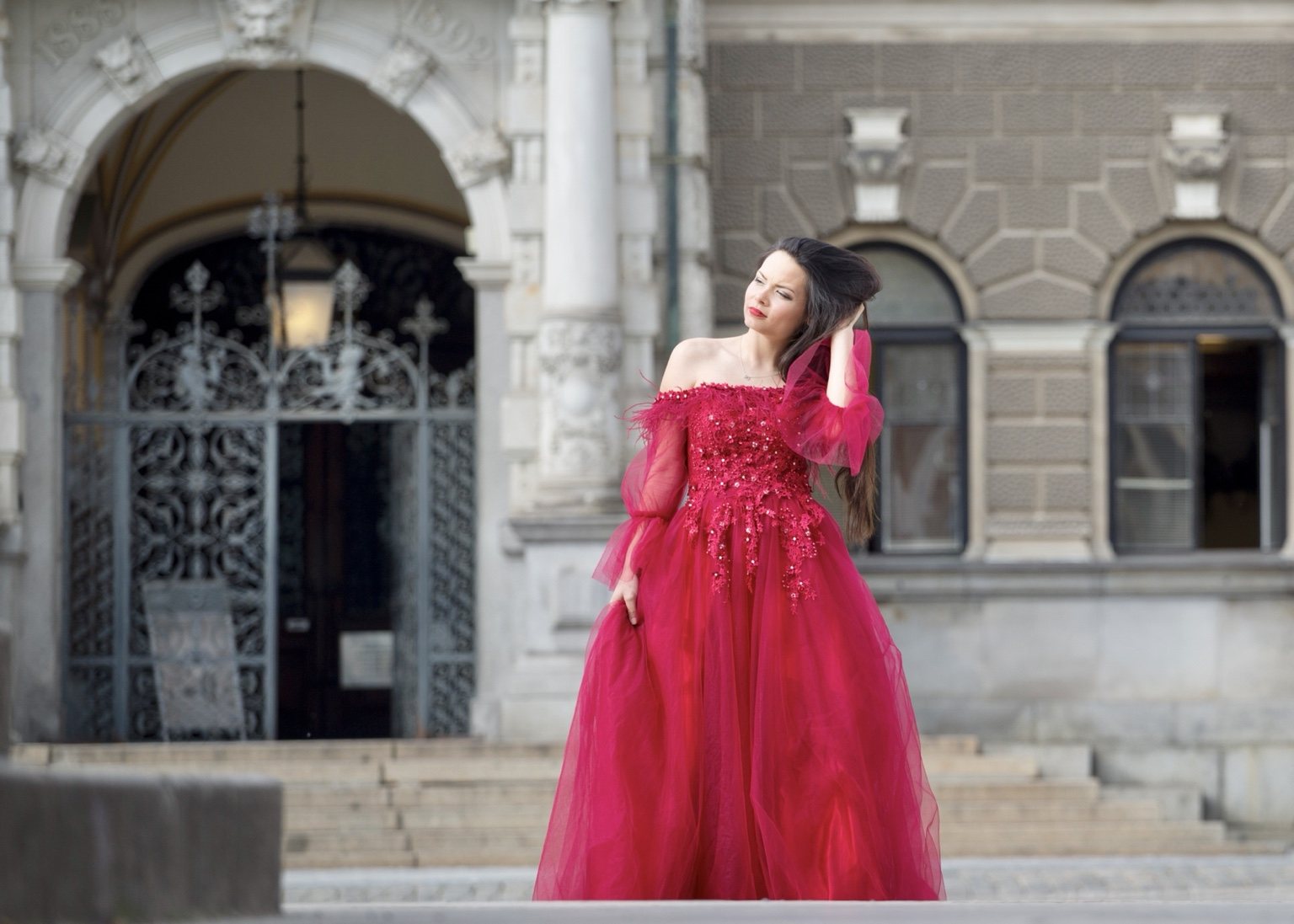 Woman in a flowing red gown posed beside historic stone architecture