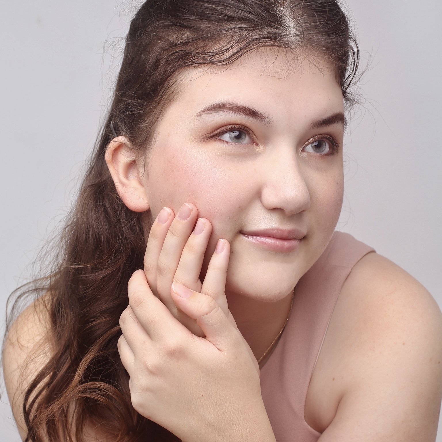 Close-up studio portrait in a blush top with hands resting gently against the cheek