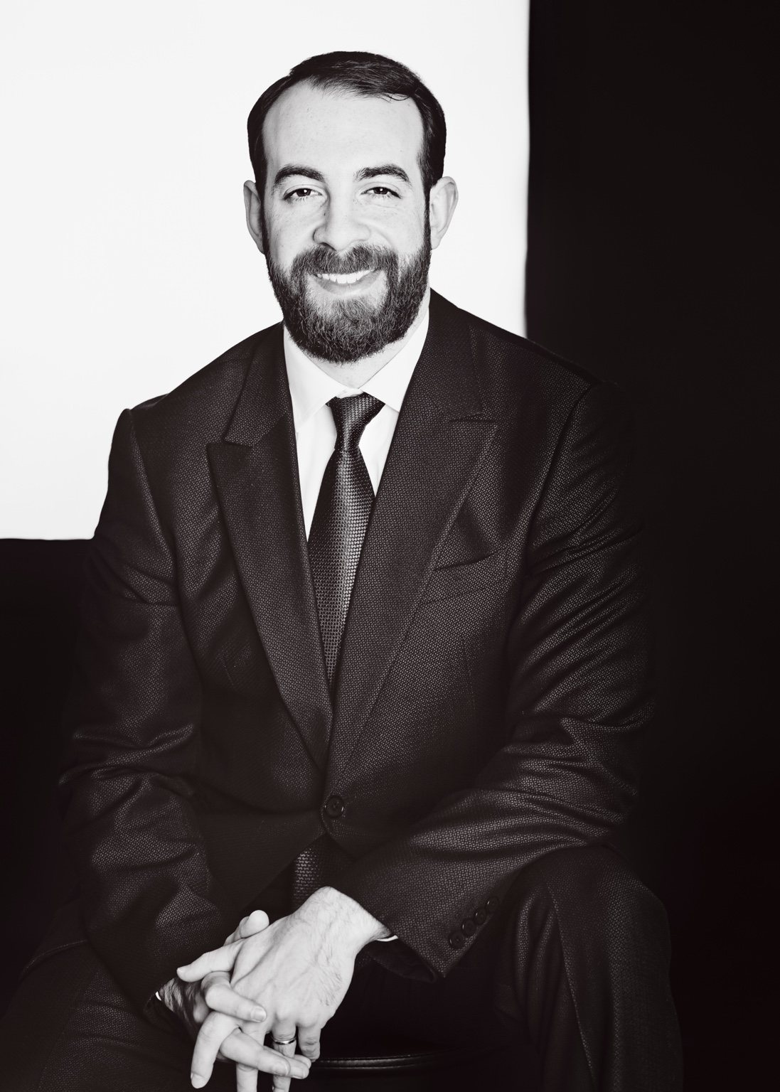 Black-and-white portrait of a smiling bearded man in a suit and tie